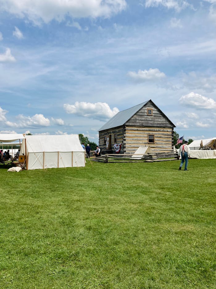 Explore a rural village setting with a traditional log cabin and canvas tents under a clear sky.